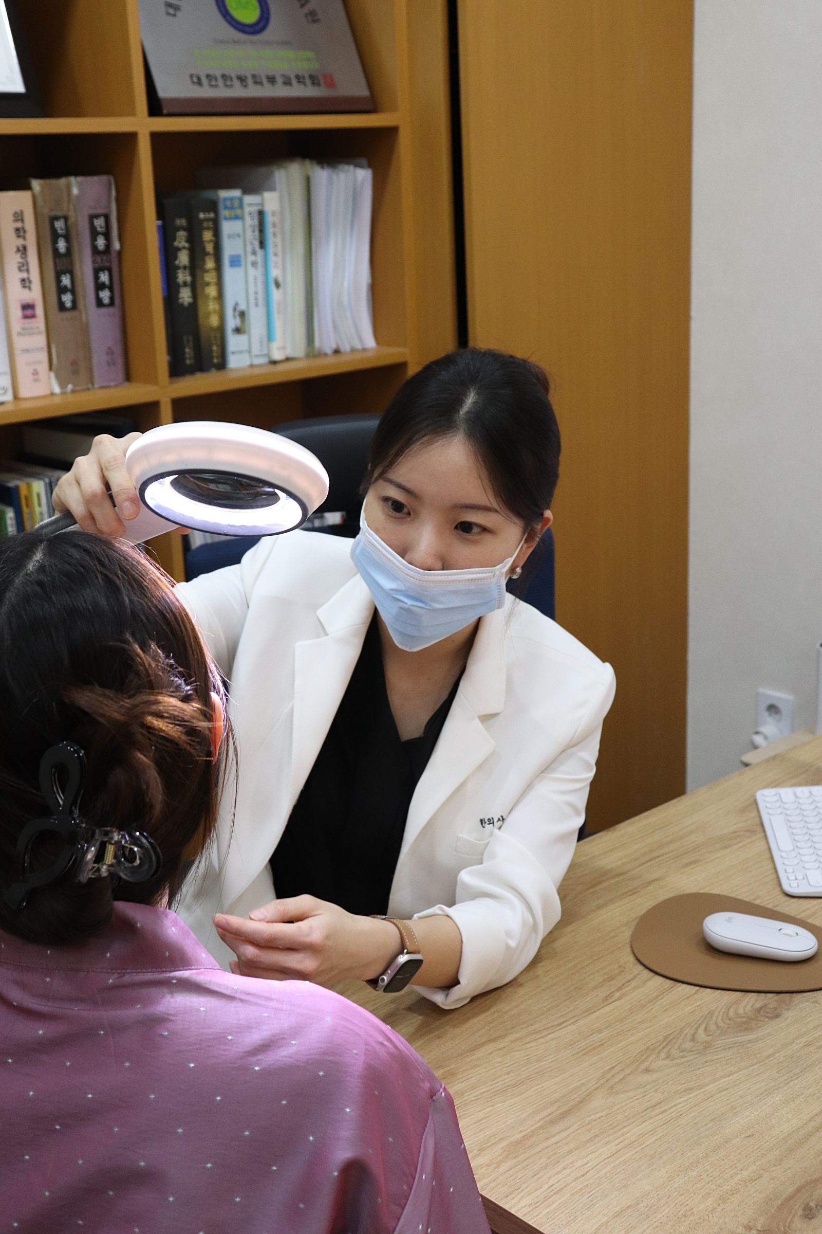 민수연 원장이 확대경을 사용해 환자의 두피 및 피부 상태를 정밀 진단하는 모습